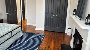Une chambre à coucher avec un lit, une porte sombre, une cheminée blanche et un plancher en bois.
