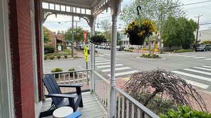 Une véranda avec un banc bleu et une petite table, donnant sur une rue où circulent des voitures et où se trouve un passage pour piétons.