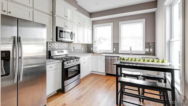 Une cuisine moderne avec des meubles blancs, des appareils en acier inoxydable et un plancher en bois.