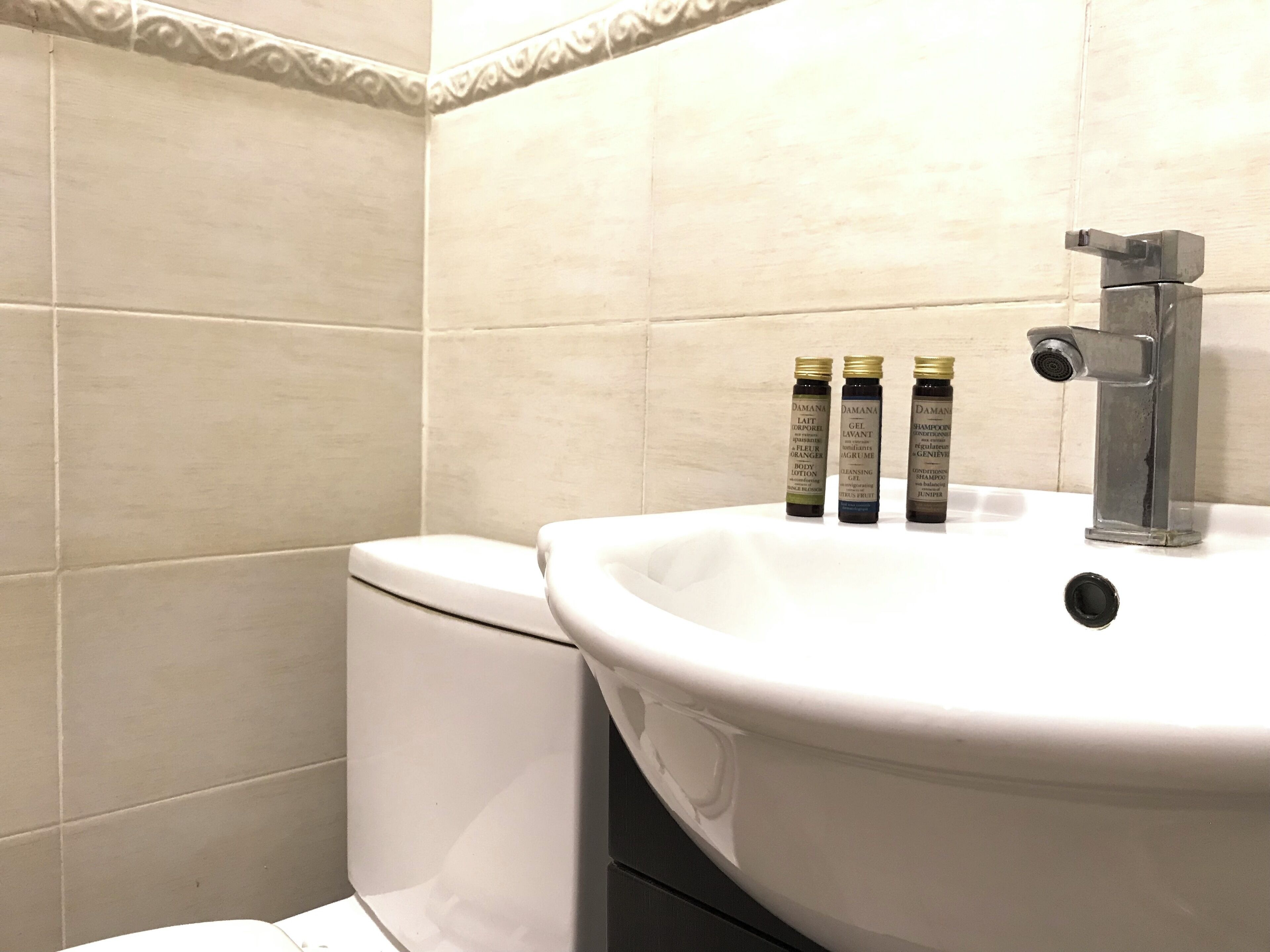 Et badeværelse med en hvid vask, en sølvarmatur og tre shampoo flasker på vasken.