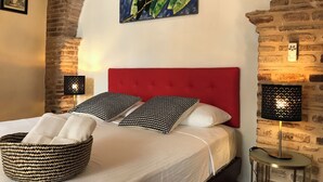 A bed with a red headboard, white bedding, and patterned pillows. There is a woven basket on the bed, a painting of toucans on the wall, and a lamp on a side table. - Paseo Colonial - Sabbatical 1 (Santo Domingo)