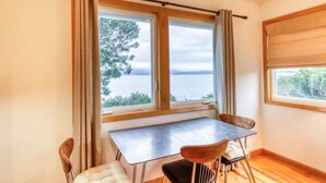 Ein Zimmer mit Tisch und Stühlen, einem Fenster mit Vorhängen und Blick aufs Meer.