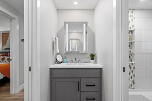 A modern bathroom with a white vanity, grey cabinets, a mirror, and a shower area with patterned tiles.