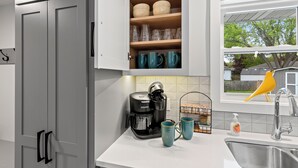 A kitchen with a coffee maker, teal mugs, and a window with a yellow bird outside. - South Endzone Suite - 5 min walk to Lambeau, 4 BR/2 BA, Pool table, Foosball (Ashwaubenon)