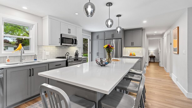 A modern kitchen with grey cabinets, stainless steel appliances, and a central island with bar stools. - South Endzone Suite - 5 min walk to Lambeau, 4 BR/2 BA, Pool table, Foosball (Ashwaubenon)