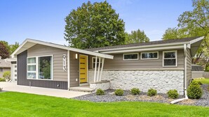 A modern single-story house with a stone facade, a yellow front door, and a well-maintained lawn. - South Endzone Suite - 5 min walk to Lambeau, 4 BR/2 BA, Pool table, Foosball (Ashwaubenon)
