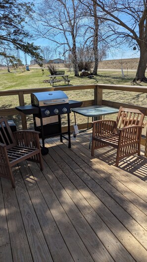 A wooden deck with a grill, two wooden chairs, and a picnic table.