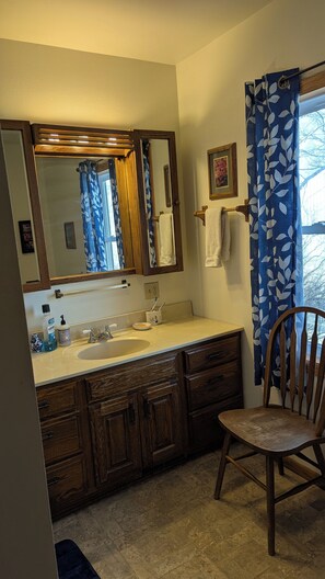A bathroom with a wooden vanity, a sink, a mirror, and a chair.