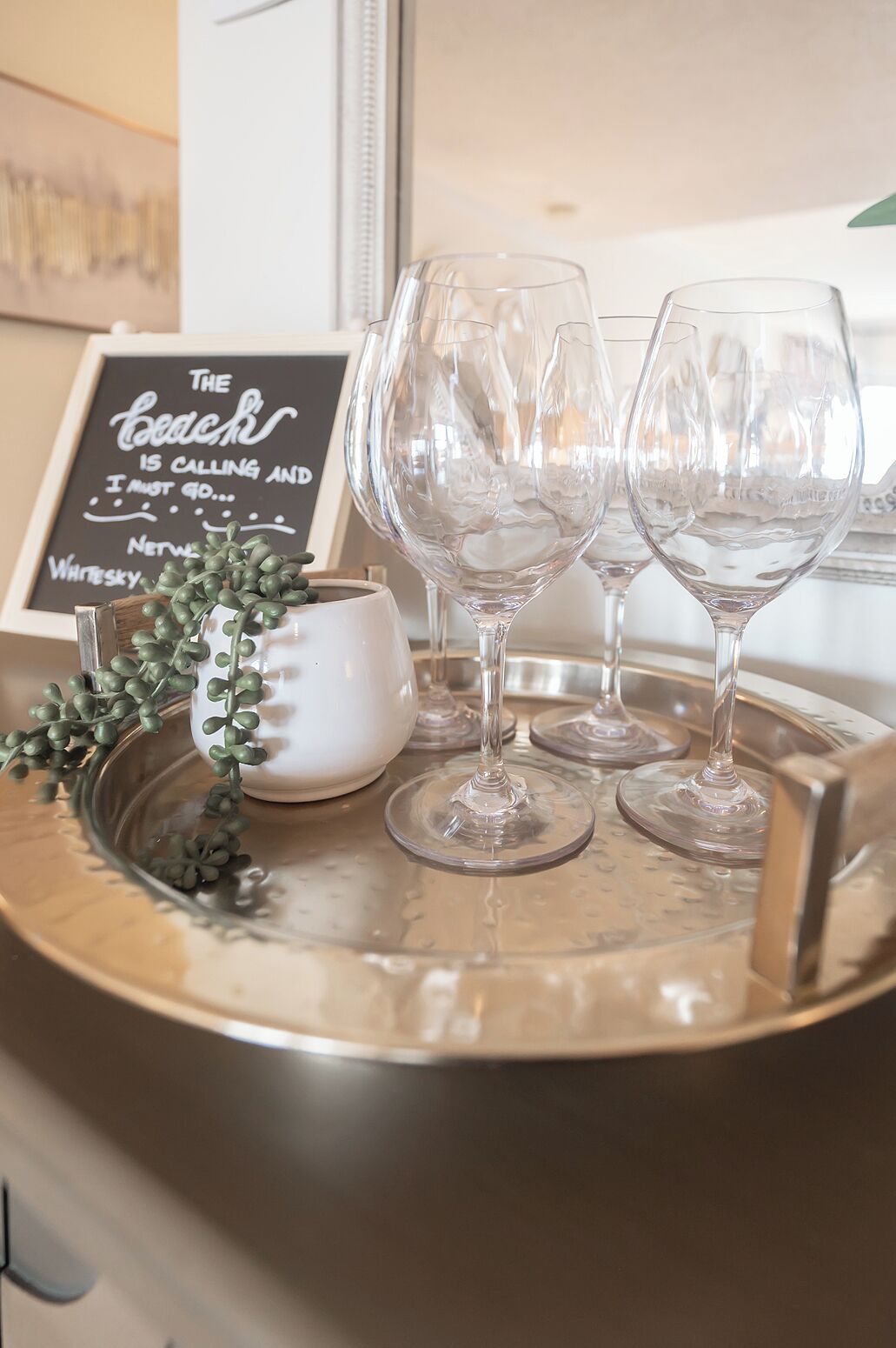 A tray with three wine glasses and a small white bowl, placed on a metallic tray with a decorative plant.