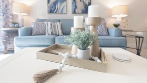 Una sala de estar moderna con un sofá, velas decorativas y una bandeja con una planta y un adorno de cuentas.