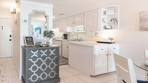 Una cocina moderna con armarios blancos, una isla central y un comedor con mesa de vidrio.
