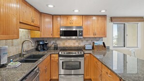 Una cocina moderna con armarios de madera, electrodomésticos de acero inoxidable, encimeras de granito y una ventana con persianas.