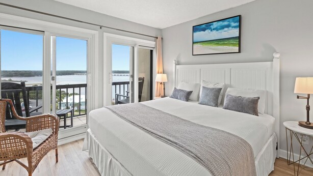A spacious bedroom with a large bed, a view of the sea, and a balcony with outdoor furniture. - Pinnacle Port,  A-708 (Panama City Beach)