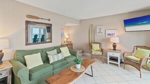 A living room with a green sofa, wicker chairs, a wooden coffee table, and a television mounted on the wall. - Pinnacle Port,  A-708 (Panama City Beach)