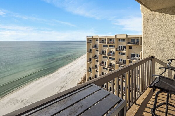 A balcony with a view of a beach and a multi-story building with balconies.