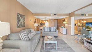 A living room with a sofa, coffee table, and a television. There is a kitchen in the background with cabinets and a microwave. - Pinnacle Port, B2-307 (Panama City Beach)