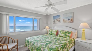 A bedroom with a large bed, a ceiling fan, a window with a view of the ocean, and two bedside lamps. - Pinnacle Port, B3-405 (Panama City Beach)