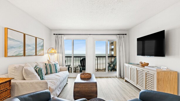 A modern living room with a balcony, a flat-screen TV, and a sofa. - Pinnacle Port, C1-401 (Panama City Beach)
