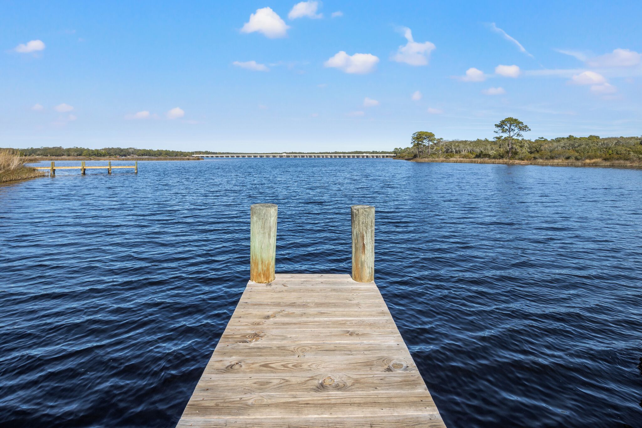 A wooden pier extending into a calm body of water with a clear sky above.
