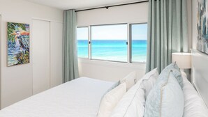 Ein Hotelzimmer mit einem Bett, einem Gemälde, einem Fenster mit Meerblick und einer Lampe.