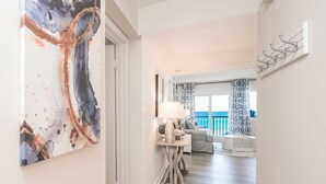 Ein Korridor führt zu einem Balkon mit Blick auf das Meer. An der Wand hängt ein Gemälde und es steht ein Kleiderständer dort.