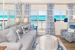 A living room with a view of the ocean, featuring a sofa, armchair, and a round ottoman. - Pinnacle Port, C3-403 (Panama City Beach)