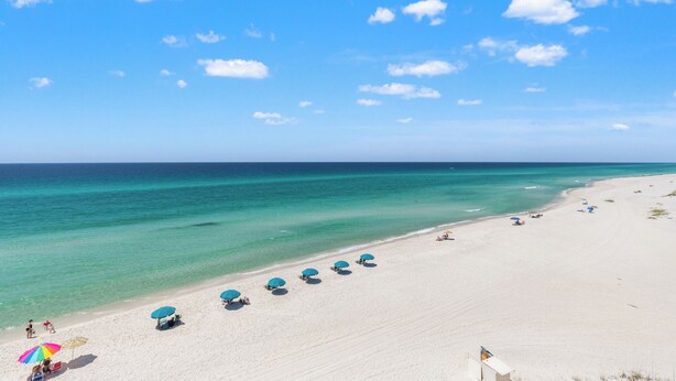 A wide sandy beach with clear turquoise water, several umbrellas, and a few people. - Pinnacle Port, C3-604 (Panama City Beach)