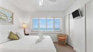 A hotel room with a bed, a television mounted on the wall, a window with blinds, and a painting on the wall. - Pinnacle Port, C3-604 (Panama City Beach)