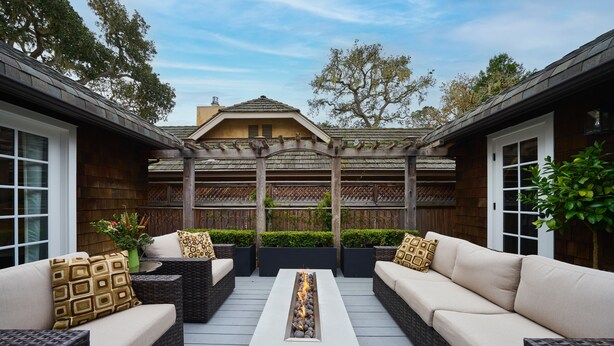 An outdoor patio with wicker sofas, a central fire feature, and a wooden pergola.