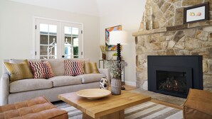 A living room with a stone fireplace, a sofa with patterned cushions, a wooden coffee table, and a vase with flowers.