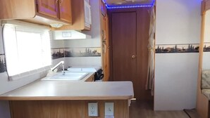 Una cocina compacta con armarios de madera, una encimera blanca y dos taburetes negros.