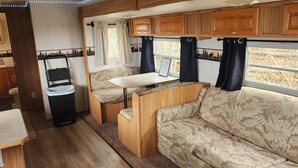 Interior compacto de una caravana con kitchenette, zona de estar y ventana con cortinas.