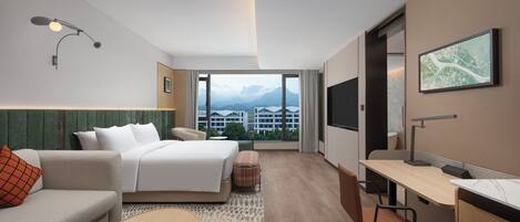 Una habitación de hotel moderna con cama, escritorio, sofá y vistas a montañas a través de amplios ventanales.