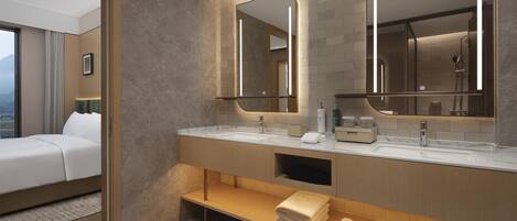 Un baño de hotel moderno con dos lavamanos, espejos amplios y una zona de ducha visible.