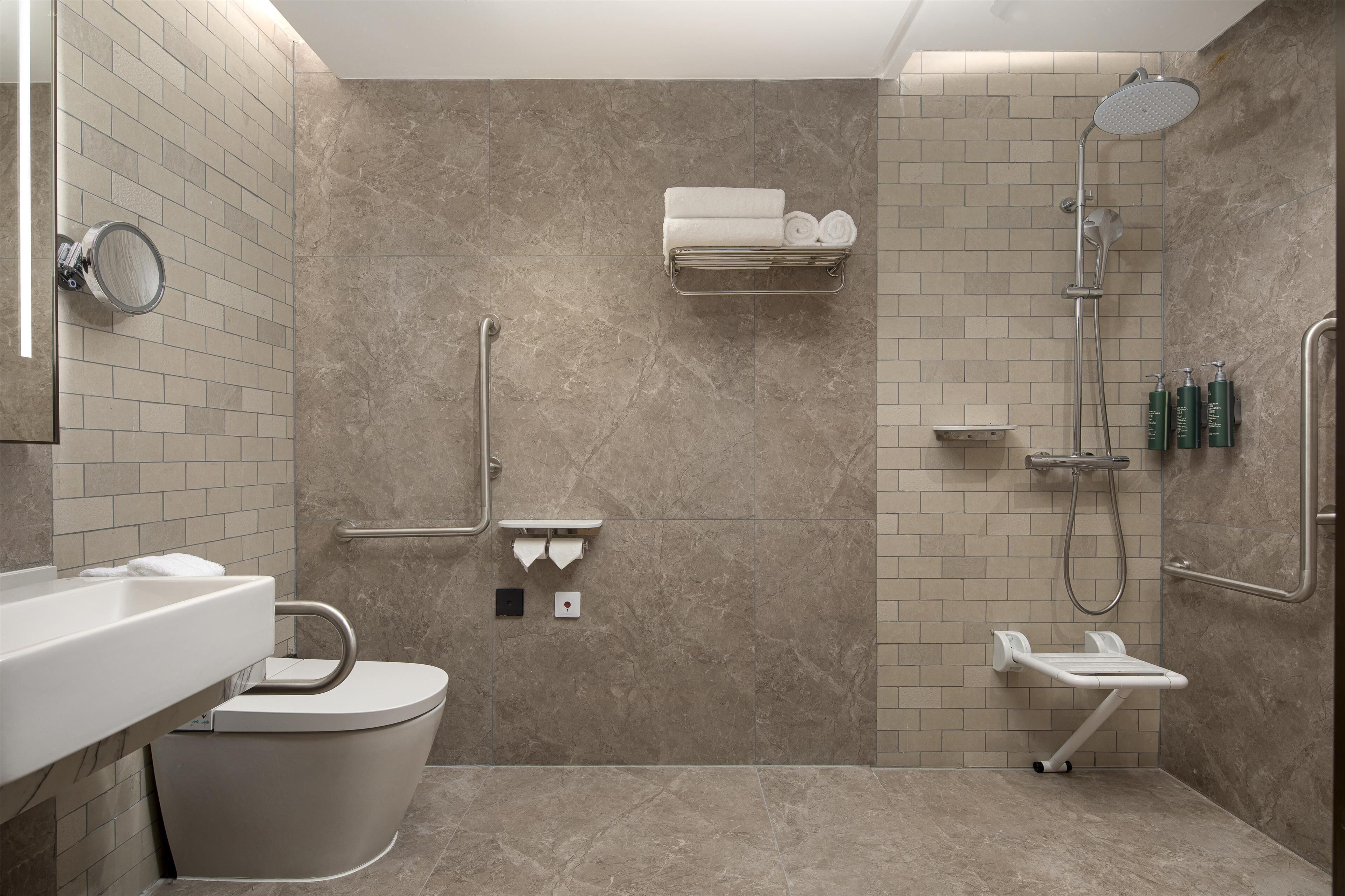 A modern bathroom with a toilet, sink, shower, and handrails.
