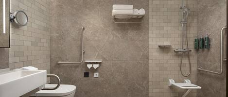 A modern bathroom with a toilet, sink, shower, and handrails.