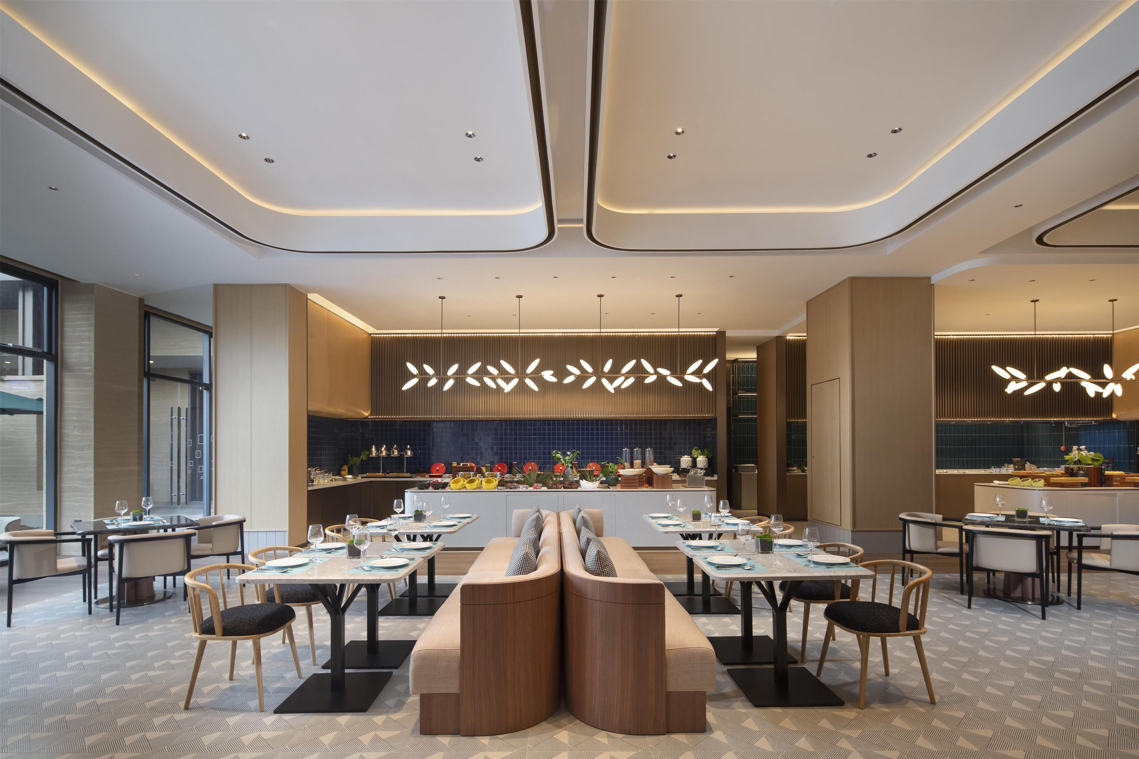 A modern restaurant with a central seating area, a kitchen in the background, and a patterned floor.