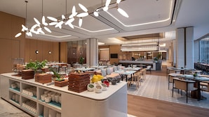 A modern hotel lobby with a central reception area, dining space, and a kitchen in the background. - Hilton Garden Inn Zhangjiajie Tianmen Mountain (Zhangjiajie)