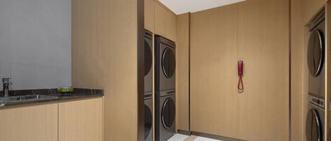 A laundry room with two stacked washers and dryers, a sink, and a red telephone.