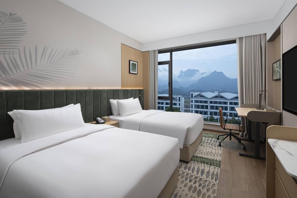 Habitación de hotel con dos camas, un escritorio y vistas a la montaña.