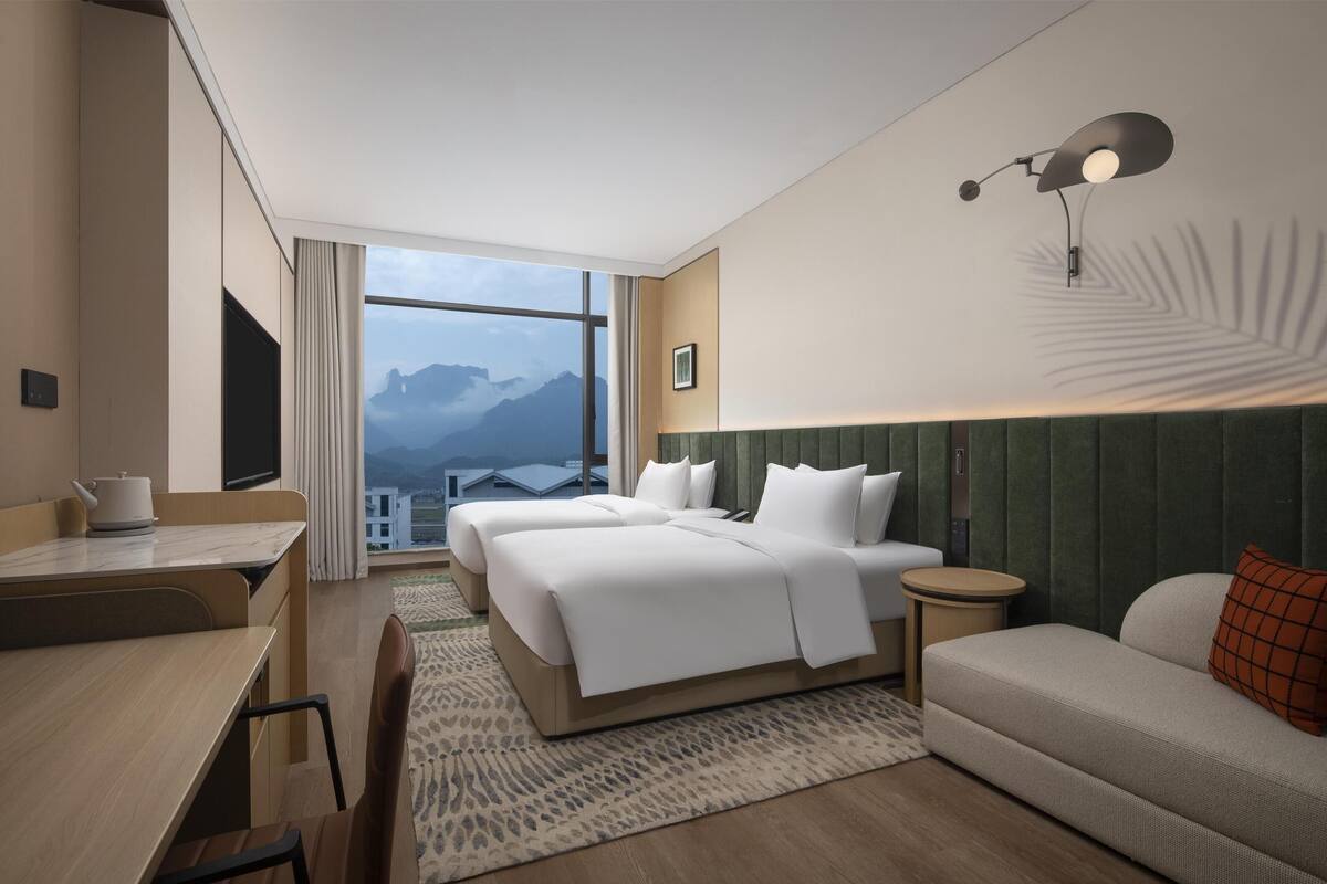 Habitación de hotel con una ventana grande, una cama, un sofá, un escritorio y una lámpara.