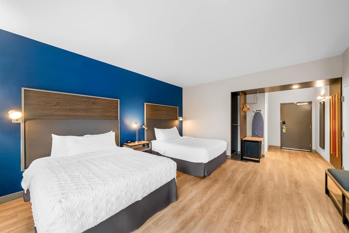 Quarto de hotel com duas camas, piso de madeira e uma parede azul de destaque.
