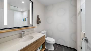 Et moderne badeværelse med en trækommode, et stort spejl, et hvidt toilet og et bruseområde.
