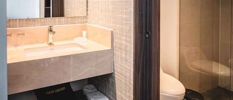 Un baño moderno con un espejo grande, un lavabo color beige, un secador de pelo y una zona de ducha.