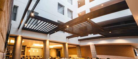 A spacious indoor area with a high ceiling, multiple seating arrangements, and a view of a building with large windows.