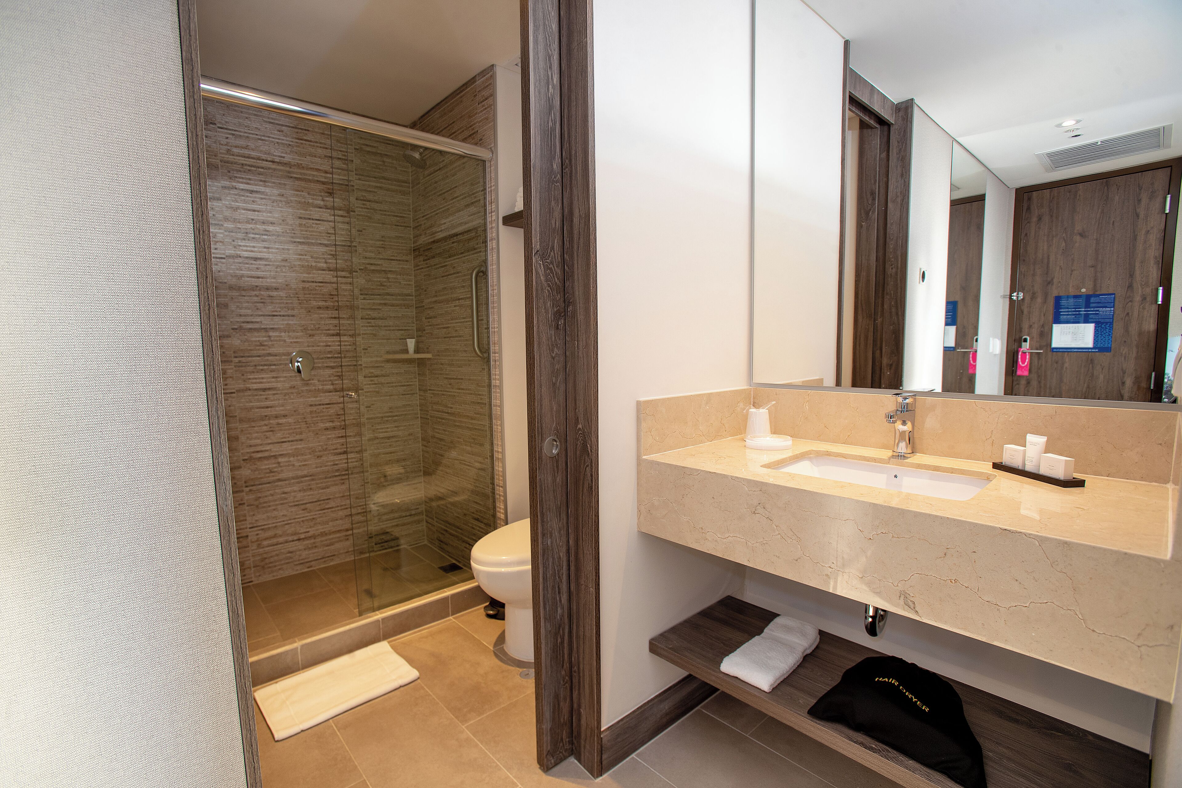 A modern bathroom with a glass shower enclosure, a sink with toiletries, and a mirror.