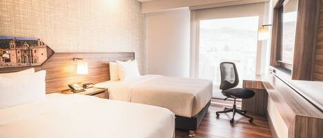 A hotel room with two beds, a desk with a lamp, a chair, and a large window with a view.