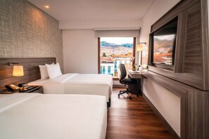 Une chambre d’hôtel avec deux lits, un bureau, une chaise et une grande fenêtre donnant sur la ville.