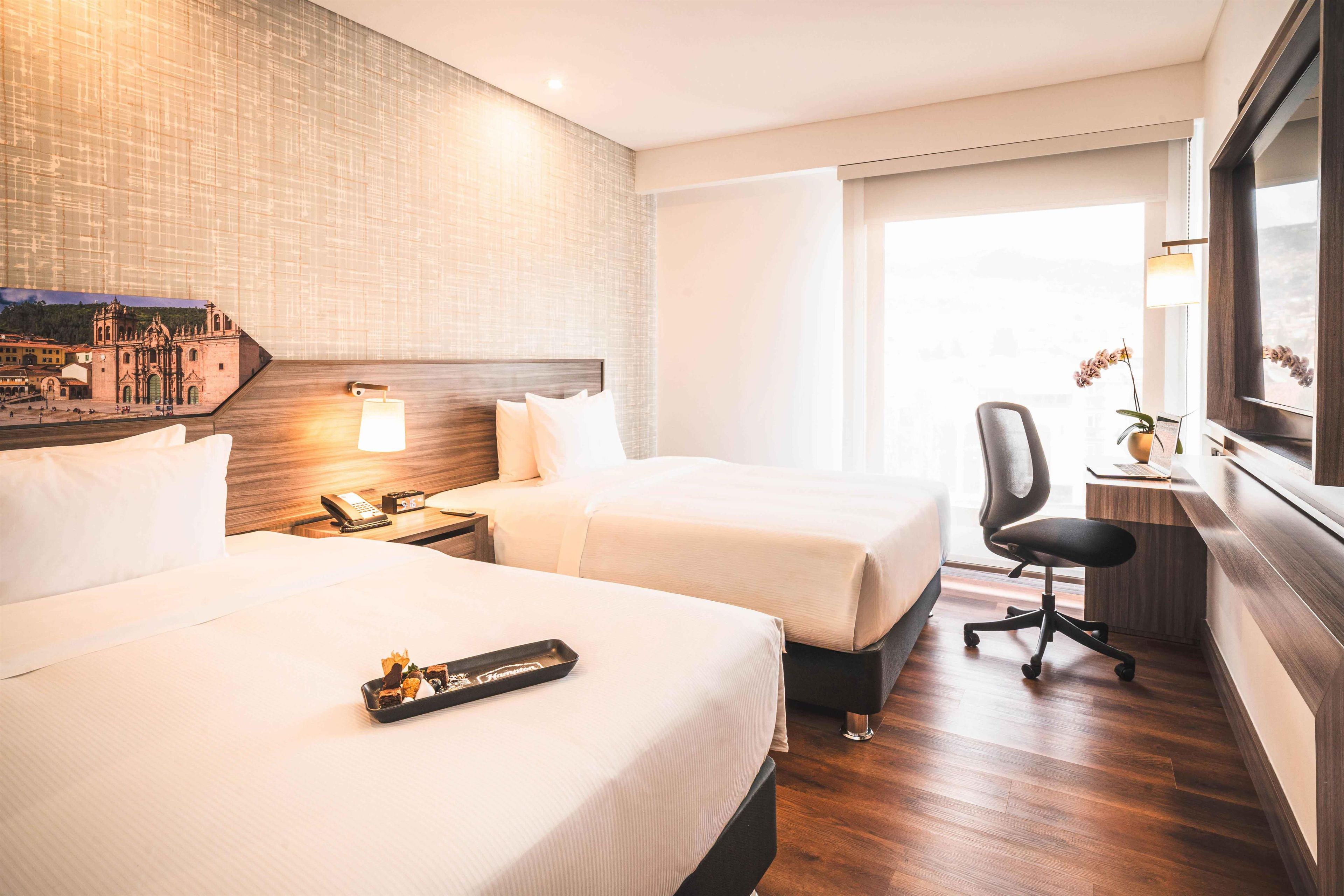 A hotel room with two beds, a desk with a chair, a phone, and a lamp.