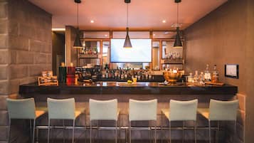 A bar area with a long counter, multiple bar stools, and a variety of bottles and glasses.